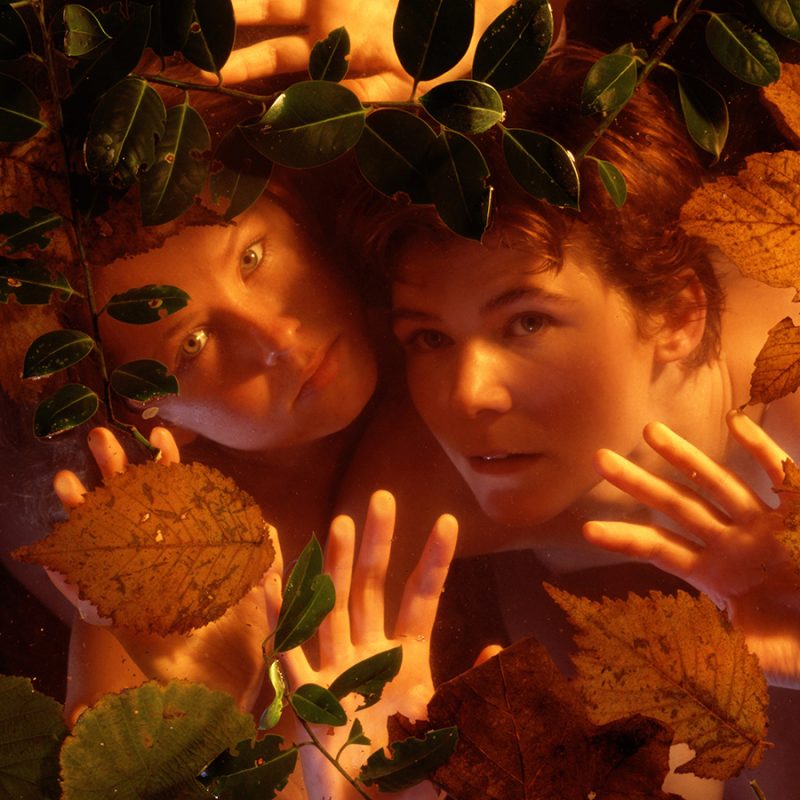 Two white woman, early 20s, under water with leaves on top. Shot from above
