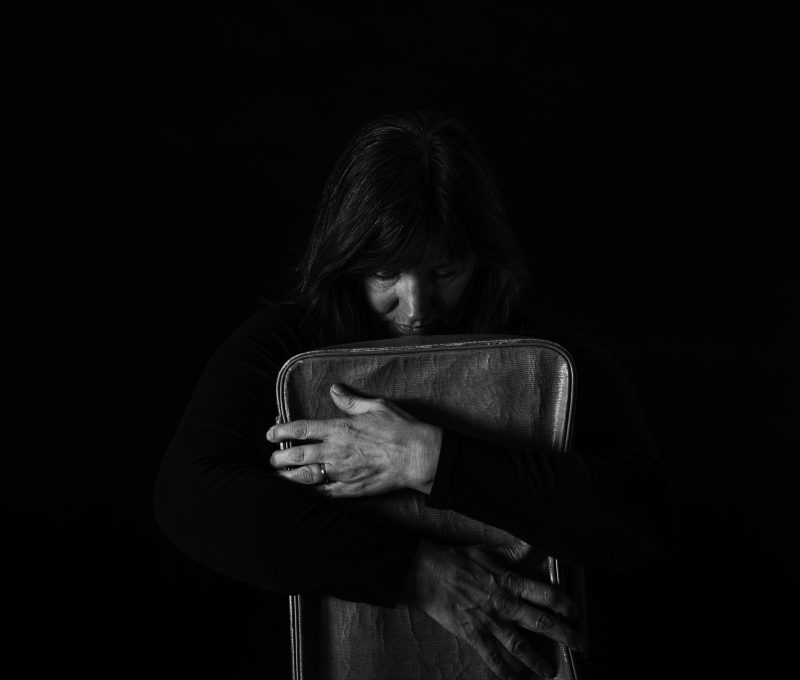 Black and white photo. Person holding suitcase, leaning face on suitcase.